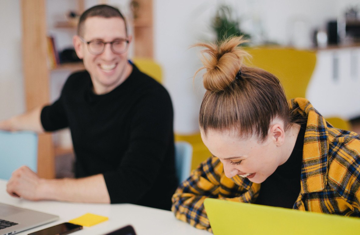 Young girl sits bent over the laptop while a man smiles and looks over her shoulder