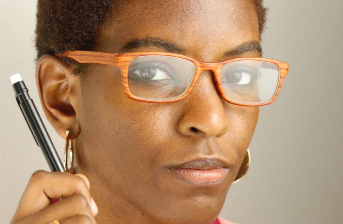 Dark-skinned woman with glasses and pen raised