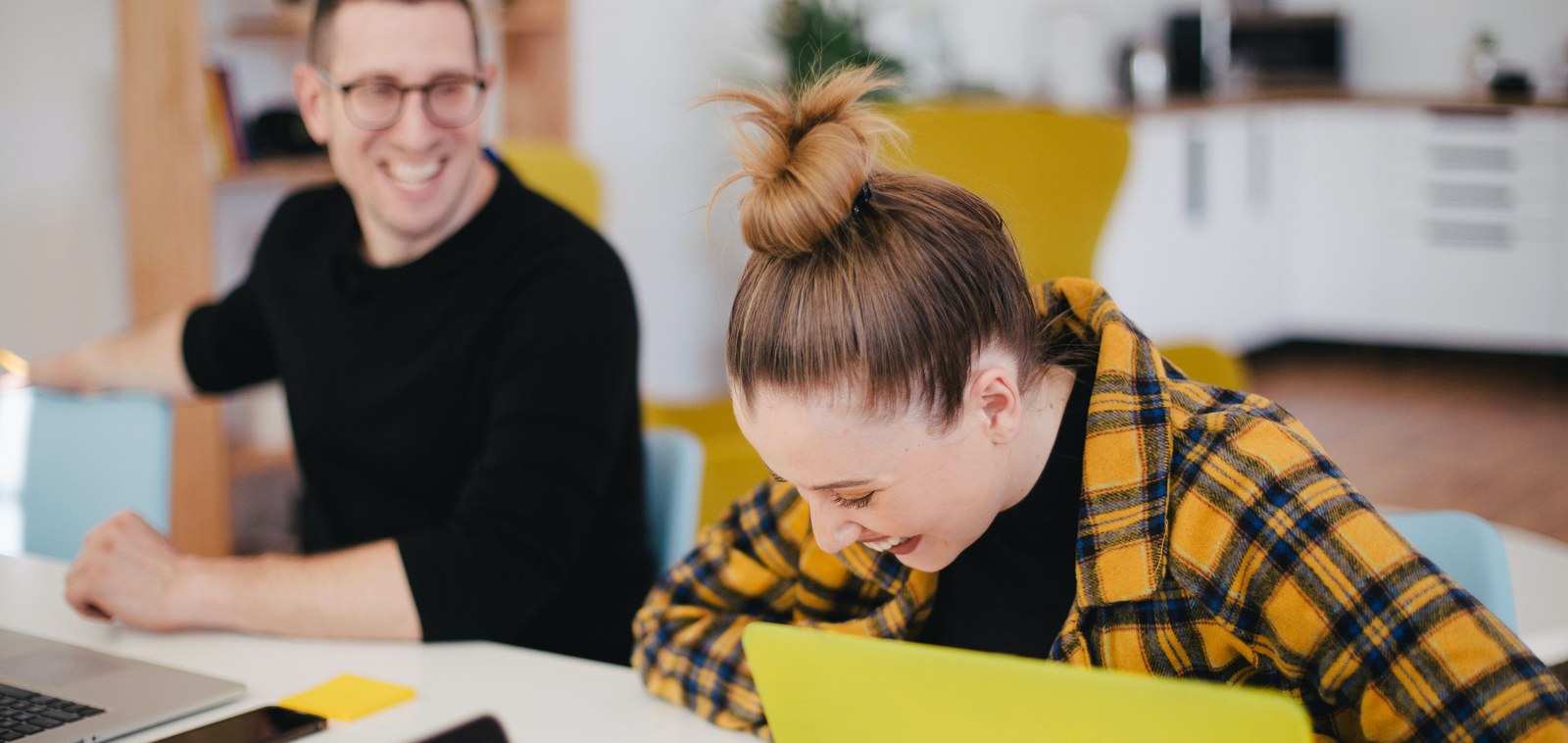 Company Teaser Bild 2.jpg Young women and young men working in IT sitting in front of her laptops, laughing.